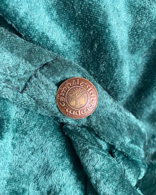 image of 4 cloaks hanging on a wall, followed by a close up of a brass button with a tree