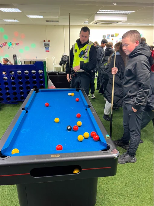 Community Police Officer playing a game of pool with young people.