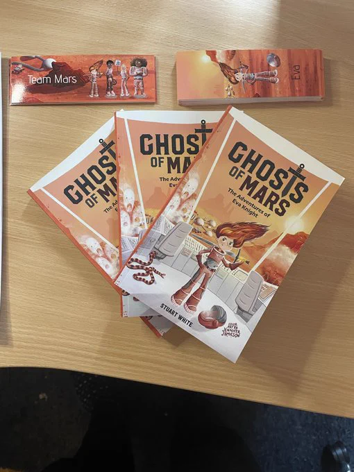 3 x Ghosts of Mars books with a pile of bookmarks on a desk.
Cover of Ghosts of Mars, illustrated by Jennifer Jamieson. Features Eva, the main character, in the centre, with her space suit on and helmet on the floor, holding a sword over her shoulder. With a martian landscape background, and the presence of ghosts at the window and an impending dust storm coming towards her. A snake slithers along the floor behind her, one of the many evolved organisms on a future Mars, ready to pounce. Illustrated by Jennifer Jamieson.