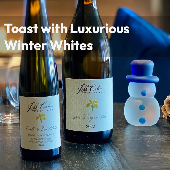 Two bottles of Jeff Cohn Cellars 2022 rhone white wines on a table with a frosted glass snowman with a blue hat and buttons with wine stems in front of a fireplace