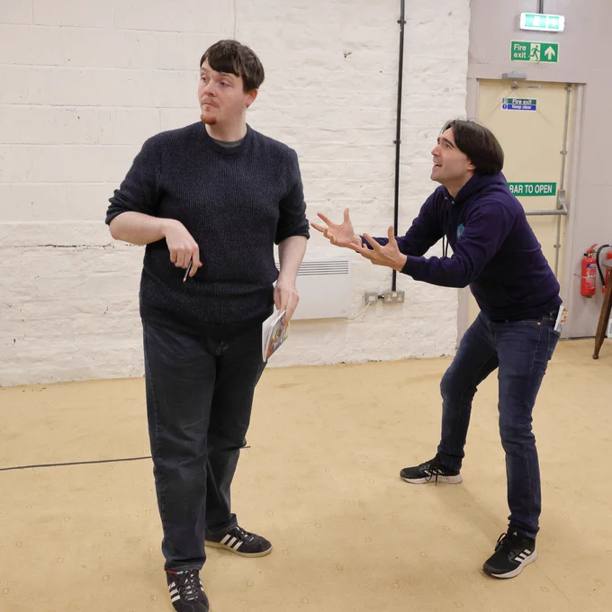 Two actors in rehearsal for Around the World in Eighty Days, one imploring the other, who seems unconcerned by his folly. Longwood Mechanics Hall, 13-16 Dec.