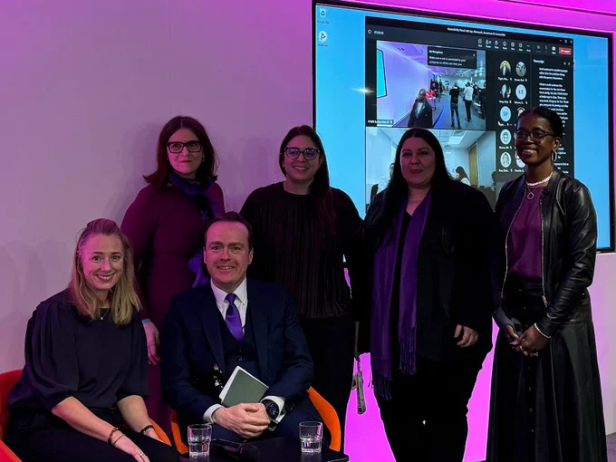 A group of people in front of a presentation screen with pink and purple lights in the background.