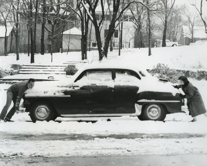 Ralph Whaley (left) and Wilmoth Marshall (right) try to move a car in the snow. Black and White photograph