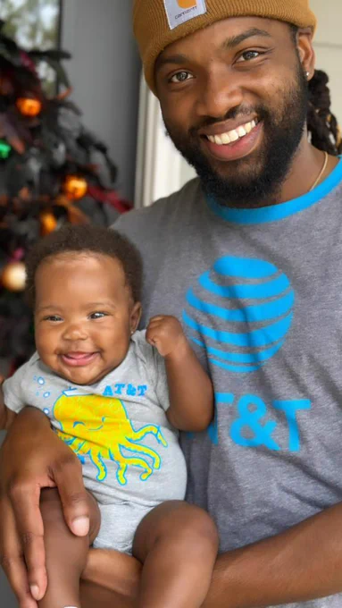Adam and his newborn in AT&T attire in front of a Christmas tree
