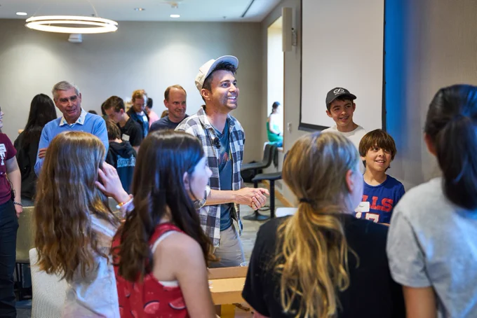 Mark Rober, wearing a baseball cap and smiling, is gathered with a group of kids from the MIT community.