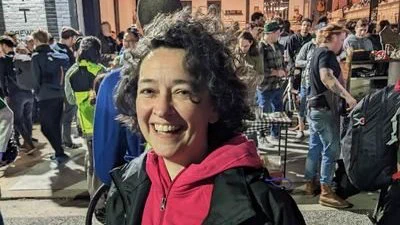 Dr. Melanie Stegman, curly haired woman smiling and wearing a hoodie and jacket by a crowd
