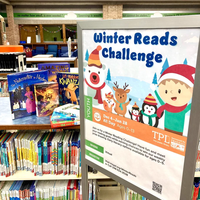 Kids library books on display next to sign with winter animals and characters for the Winter Reads Challenge at the library