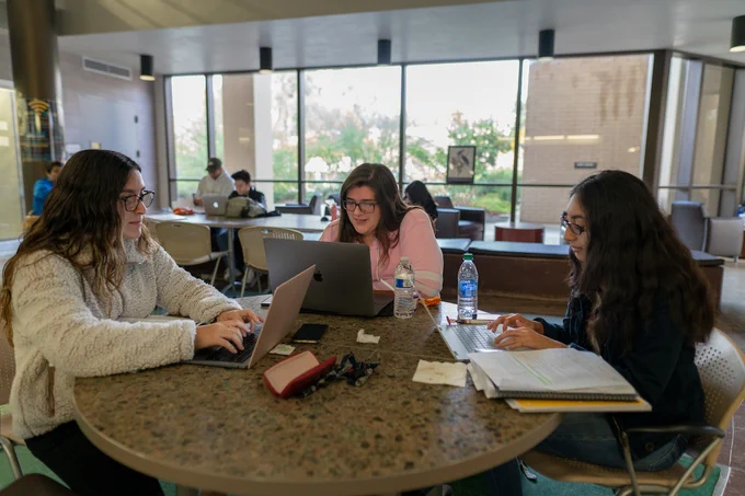 Students gathered around table in Library studying with notebooks and computers