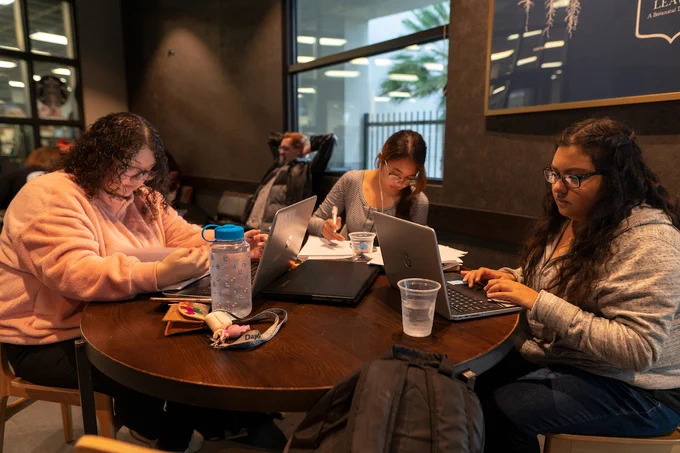 Students gathered around table in Starbucks studying with notebooks and computers