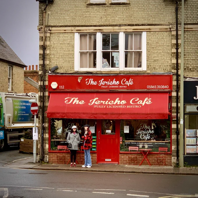 The Jericho Cafe on a street corner on the Main Street through a pretty part of Oxford. The cafe has a red frontage, door and canopy.