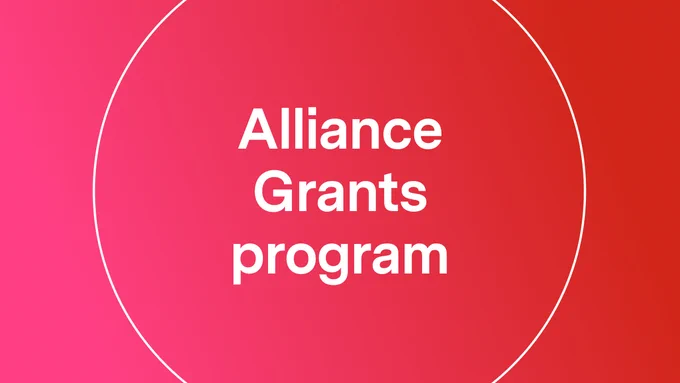 IMAGE: Bright red background. In a white, thin-lined circle, we see big white lettering inside saying: "Alliance Grants program".