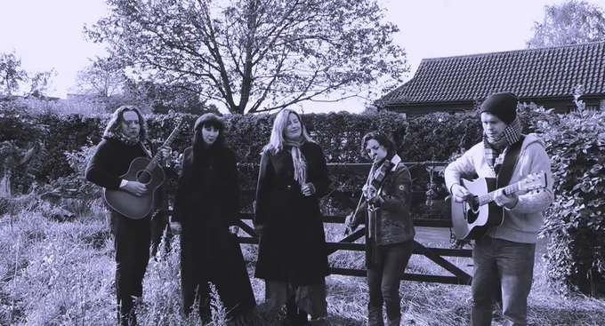 Black and white screenshot of A Winter Union playing music outside in a field, with a gate, building and trees in the background. This is taken from the video from "Minstrels", which you can hear on their album, "Sooner After Solstice". 