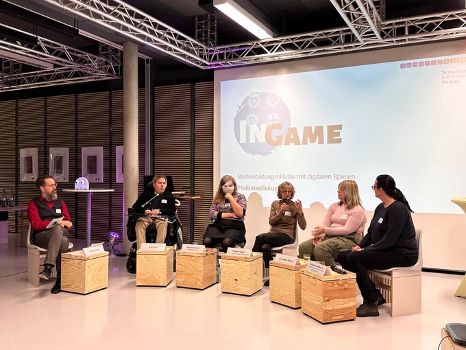 Sechs Menschen diskutieren auf einem Podium. Im Hintergrund Schriftzug: „InGame“. 
