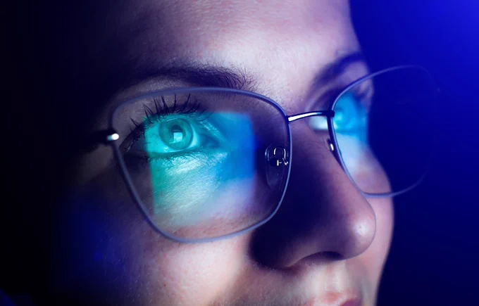 a close up of a woman's face as the content on a projection screen is reflected on her glasses.
