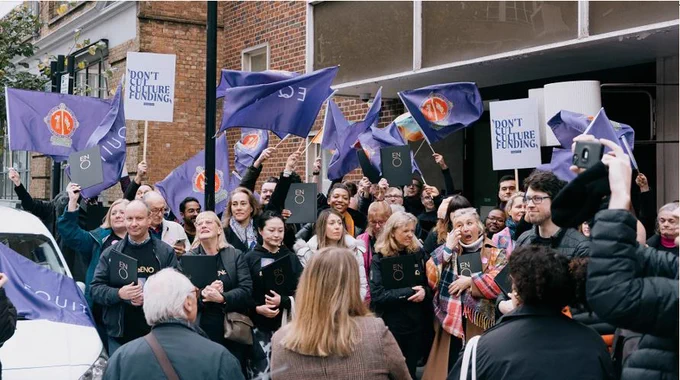 Photo shows ENO chorus protesting outside Arts Council England offices when original cuts were announced