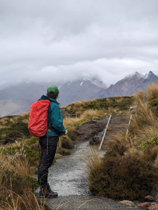 photograph of woman in waterproofs looking into the distance at a volcano appearing from behind a cloud