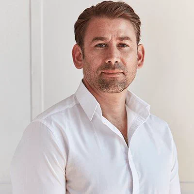 A man in a white shirt standing in front of a white wall.