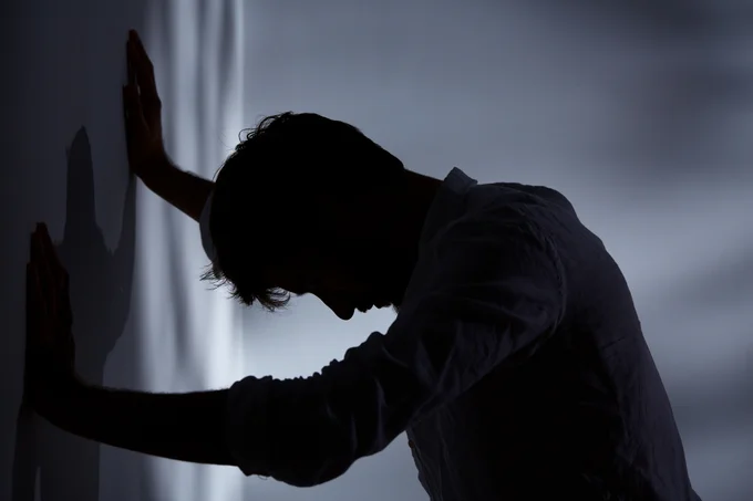 A mean leaning his hands against a wall with his head hung low. 