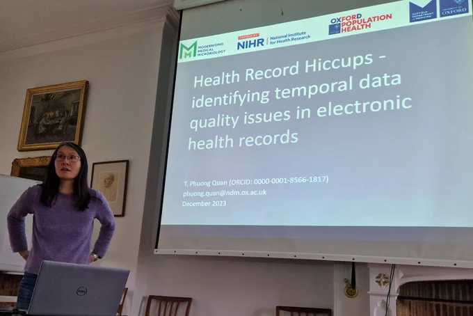 Researcher standing in front of a screen with a slide entitled "Health record hiccups - identifying temporal data quality issues in electronic health records"
