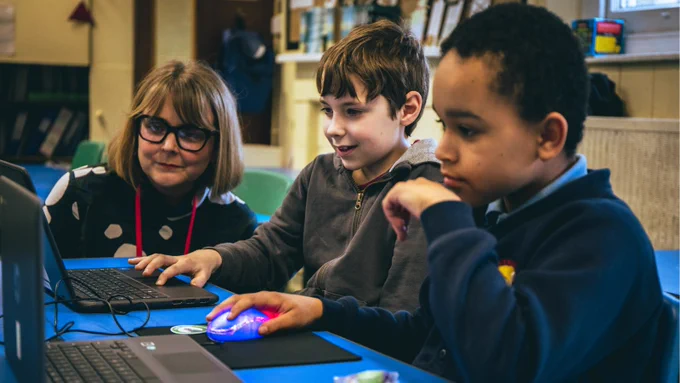 An adult watching two young learners engaging with laptops at a Code Club.