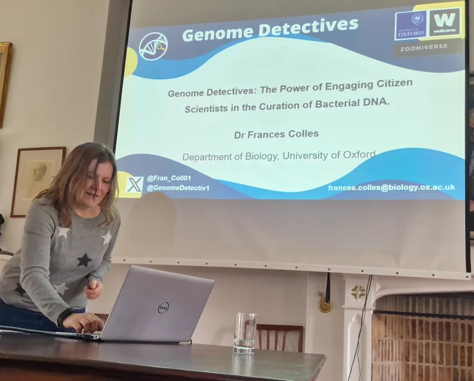 Researcher in front of a projector screen with the title "genome detectives"
