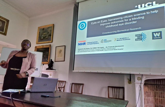 Researcher standing in front of a screen with a slide entitled "Eyes on eyes: harnessing citizen science to help improve outcomes for a blinding childhood eye disorder"