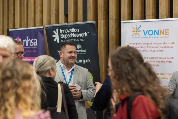Two people in front of roller banners for nhsa, Innovation SuperNetwork and VONNE.