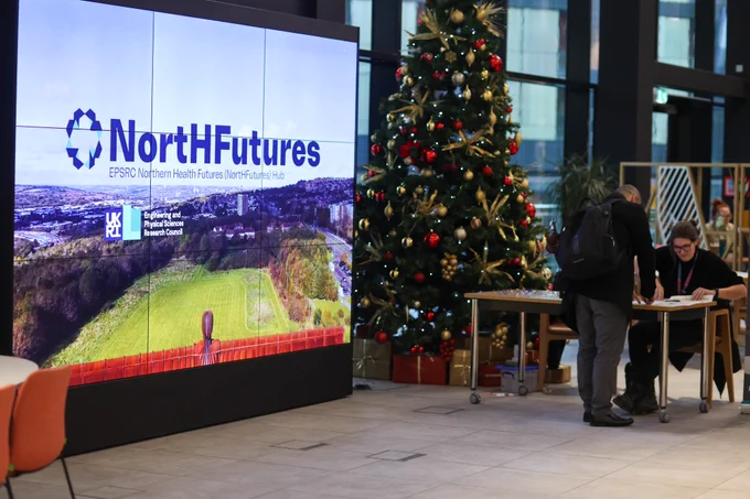 A screen (on the left) saying NortHFutures next to a Christmas tree (on the right) and someone checking someone in at a desk. 