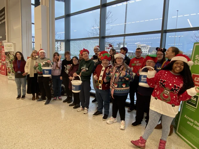 Upmo Music Group Christmas caroling at Asda, they're wearing festive attire and holding their carol sheets.