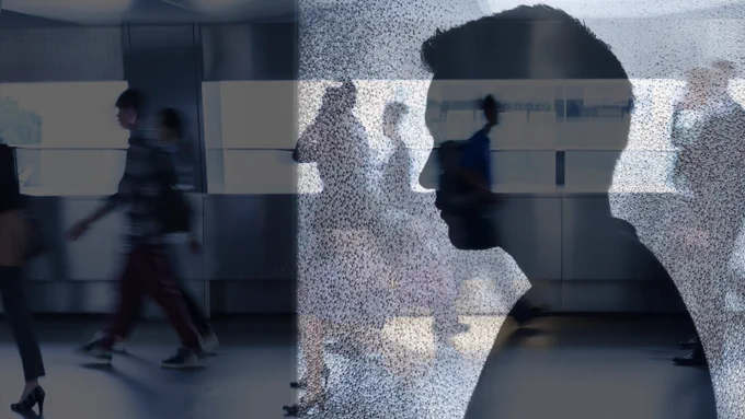 Photo of a male side profile/silhouette with people walking in a dark background. 