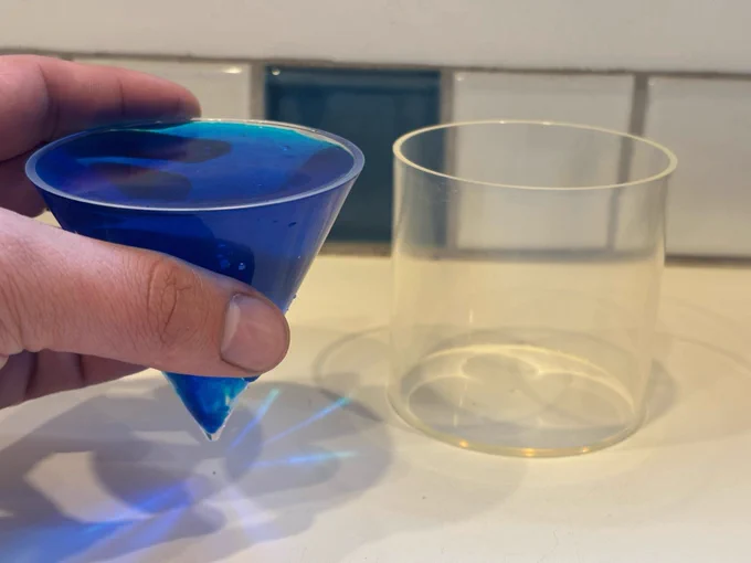 A cylinder and cone of equal heights and diameters. The cone is filled with blue liquid (water and food coloring).