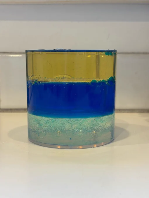The fourth photo in the sequence. The cylinder is filled with three equal layers - yellow, blue, clear (from top to bottom).