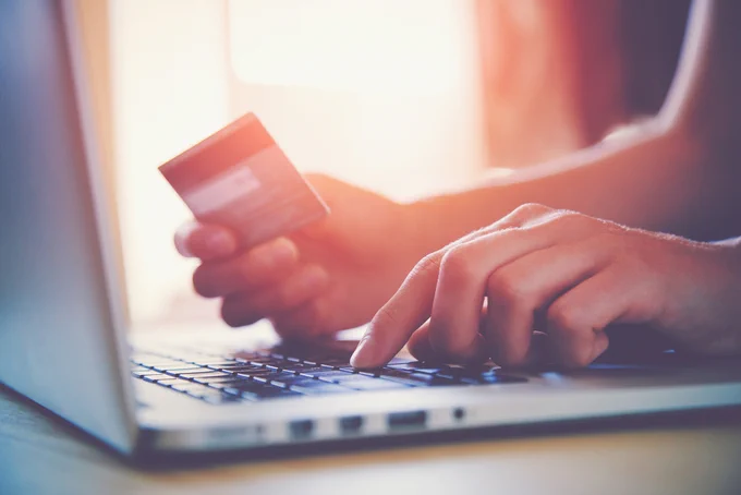 Hand holding a credit card while typing on a laptop.