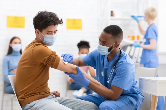 A male doctor preparing to administer the SARS-CoV-2 vaccine to a male patient. 