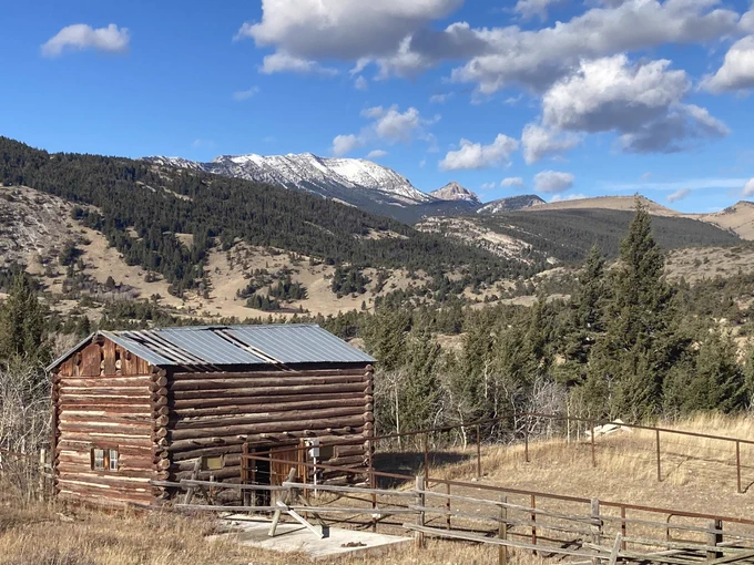 Wooden cabin stands in foreground with Rocky Mountains covered in snow behind it