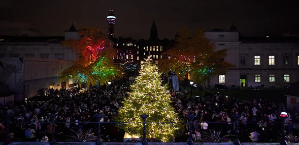 Night-time outside UCL buildings, showing the lit-up Christmas tree and other decorations