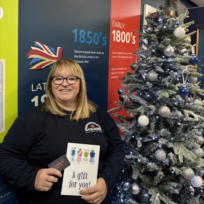 A woman in a black 'Squire' t-shirt smiles while holding a 'A gift for you' envelope, next to a Christmas tree with blue and white decorations; historical timelines are visible in the background.