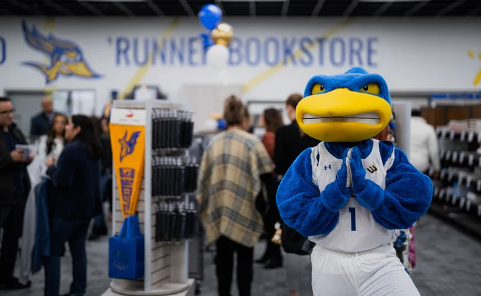 Rowdy posing in front of `Runner Bookstore sign on wall as others walk through the store