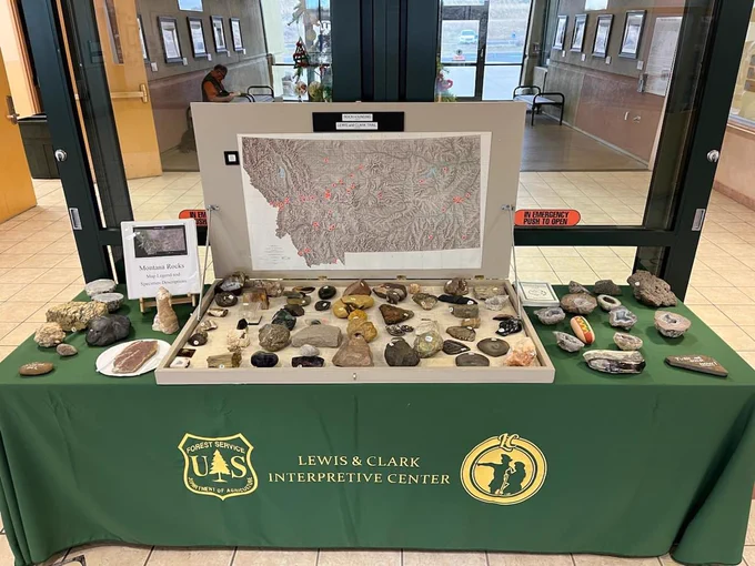 Table full of rocks from around Montana with a guidebook. A conspicuous hot dog sits on the table and is part of the exhibit.