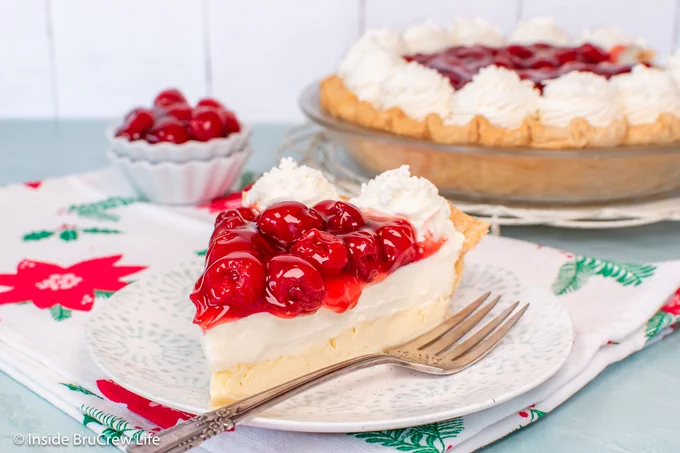 A slice of cheese pie with cherries on a plate.