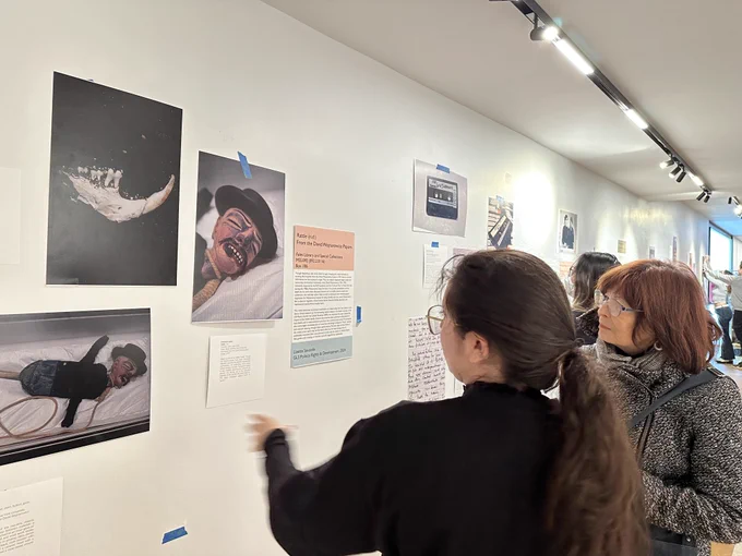 A female student with brown hair and glasses explaining an art piece to Dean Mostov with red-brown hair who is wearing a black and white tweed jacket and glasses