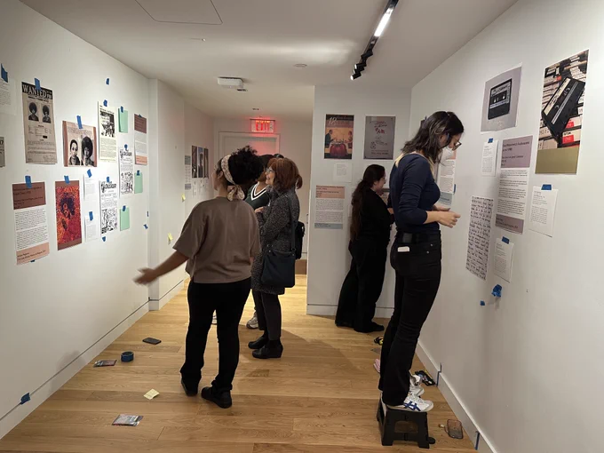 Three ladies standing and looking at artwork hung on a white wall with blue tape and two ladies hanging art with blue tape on the opposite wall