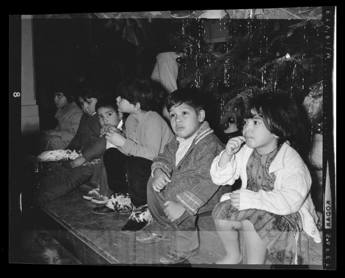 A black and white photo of a row of six children sitting in from of a Christmas tree in 1965