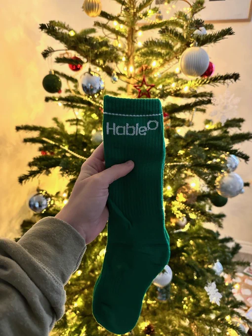 Green socks held up in front of a Christmas tree, with lights twinkling. 