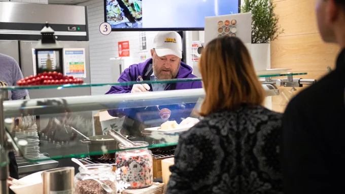 A person prepares food behind a counter for an individual.