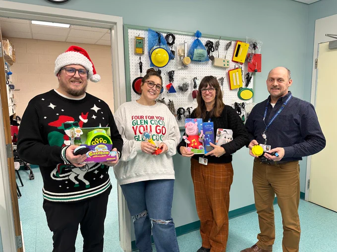 Brilliant Labs team members and Janeway staff stand holding adapted toys in front of a wall of switches.