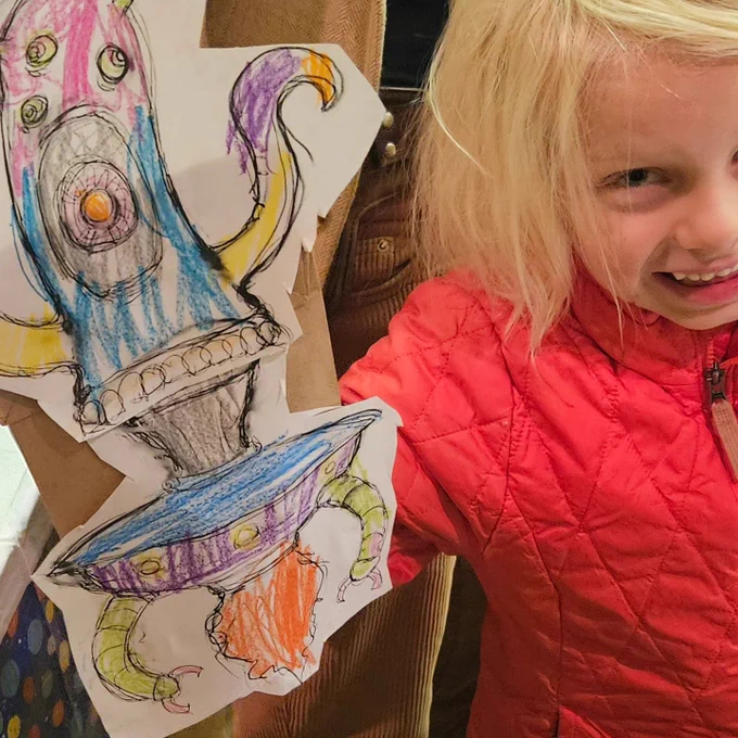 Kid smiling with their brightly colored paper bag puppet