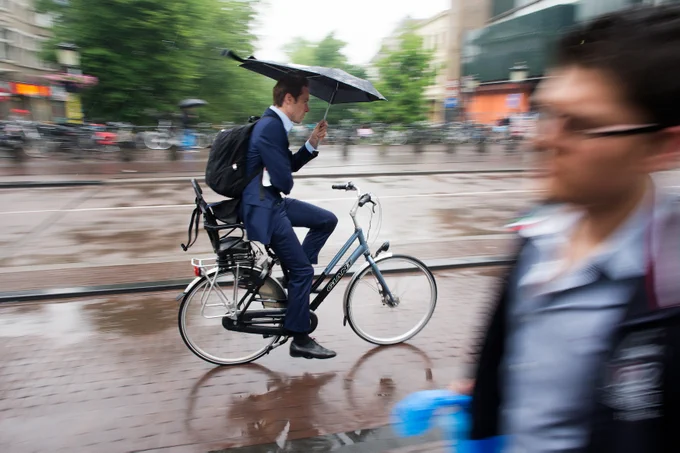 Man in a suit on a bicycle holding an umbrella in Utrecht