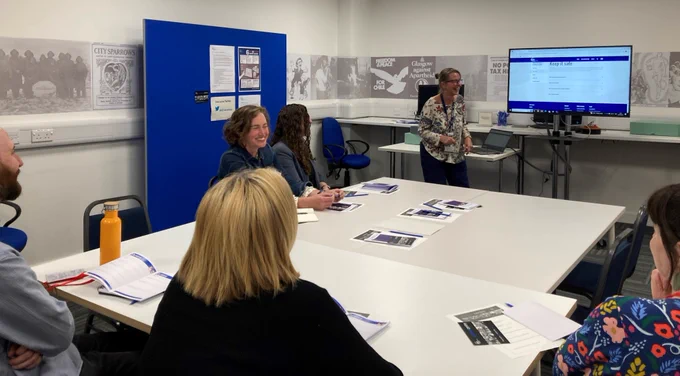 A group of people sat around a big table in the Archive Centre reading room facing a screen where archivist Kirsty shows them the Social Enterprise Archiving Toolkit