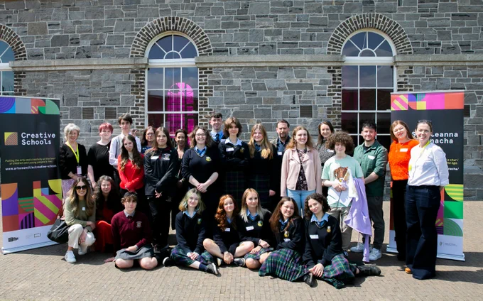 A group of students and teachers stand outside in front of a stone building between two Creative Schools Pop up signs